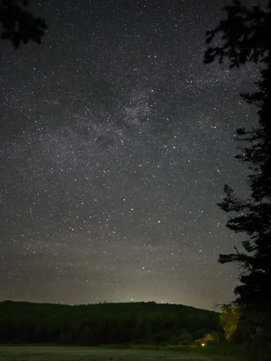 A small house sits on a pond beneath a vast array of stars.