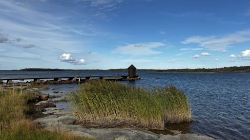 Photo from the shore of a small bridge leading out to a tiny little house on the water.