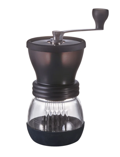 Picture of the Hario Ceramic grinder on a white background. It's a two part grinder - the top is a black plastic hopper with a horizontal handle for grinding. The bottom is a glass bowl that screws into the top, with black silicone cover over the base.
