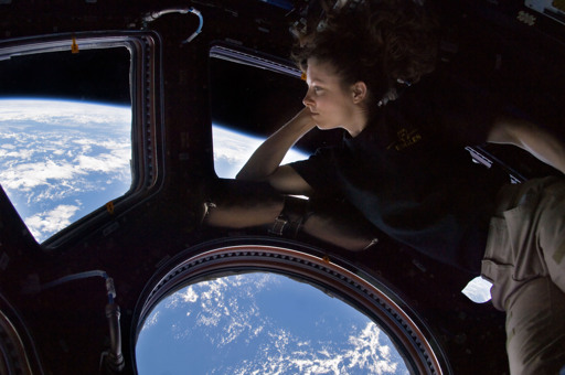 Flight engineer Tracy Caldwell Dyson leaning against the Earth-facing side of the Cupola of the ISS. The Earth is visible in the windows.