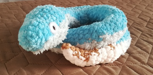 Blue crocheted snake with a pale underside and brownish tail. Curled up. Pale blue button eyes.