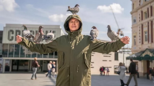 man in green jacket with pigeons on him