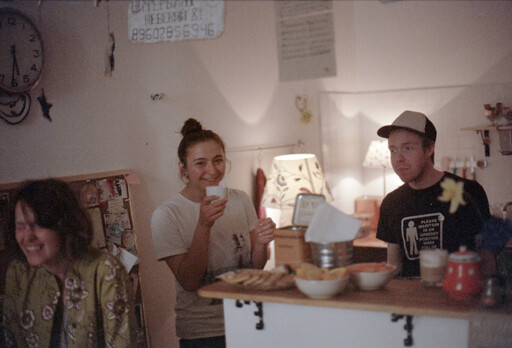 3 people right next to the counter at a cafe. They have different looks on their faces, one is smiling and looking on the camera, one is laughing with eyes closed, one is looking the other way.